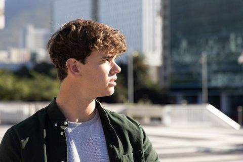 Thoughtful teenage male looking toward skyline in sunlit urban plaza wearing green shirt
