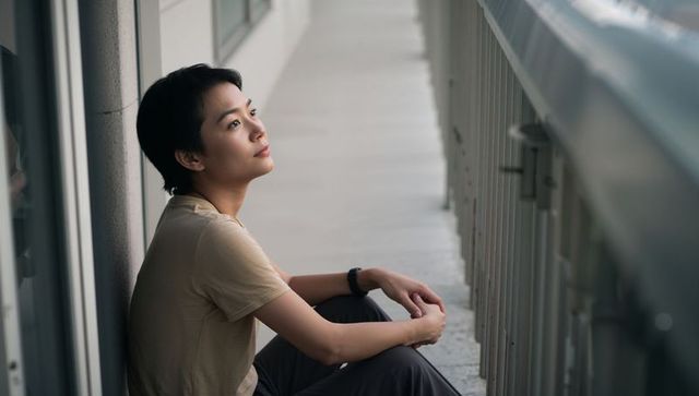 Young woman sitting and reflecting on balcony corridor with soft daylight contemplative mood
