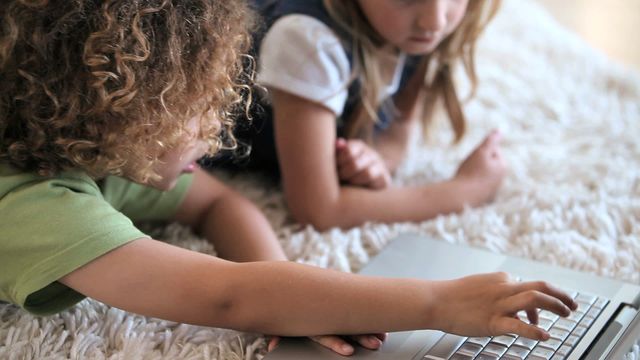 This scene shows two children engaging with a laptop and tablet while lying on a comfortable carpeted floor. Perfect for illustrating home learning environments, modern education technology, and children's interaction with digital devices. Useful for campaigns or content focused on family, education, or tech markets.