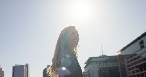 Young woman smiling and standing in sunlit city plaza with lens flare and skyline