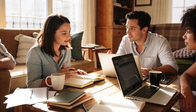 Cozy home coworking team brainstorming around laptop and notebooks in living room