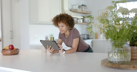 Young woman leaning on kitchen island using tablet in bright minimalist home workspace