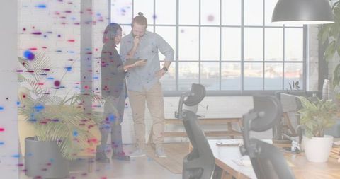 Two coworkers reviewing tablet in modern plant-filled office with harbor view