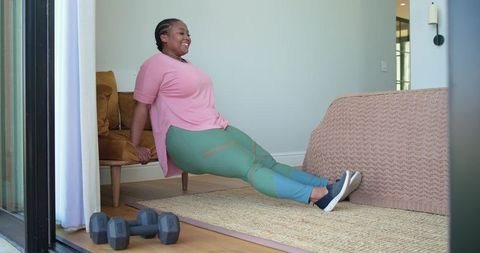 Plus-size woman performing triceps dips on bed edge during home strength training session