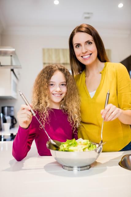 Mother assisting daughter in making salad in kitchen
