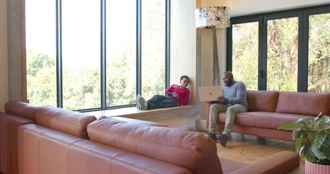 African american father and child using laptop and tablet on window seat in living room