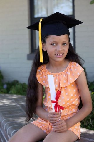 Young girl graduate wearing mortarboard holding diploma in garden celebrating milestone