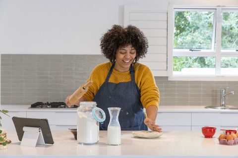 Smiling woman shaping dough and baking bread on kitchen island with tablet recipe
