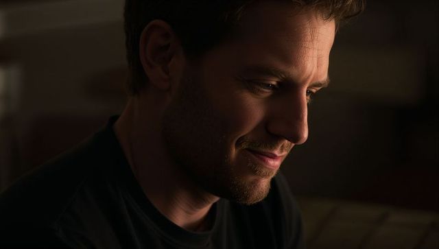 Contemplative smiling man bathed in warm low-key light, intimate close-up portrait