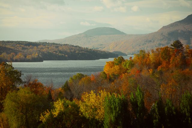 This image showing a serene lake surrounded by vibrant autumn trees and mountains in the background. Ideal for nature-themed websites, travel blogs, and seasonal promotional materials. Perfect for depicting Fall scenery and tranquility in outdoor or environmental contexts.