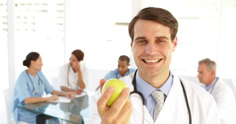 Doctor Advocating Healthy Lifestyle Holding Green Apple in Hospital - Download Free Stock Images Pikwizard.com