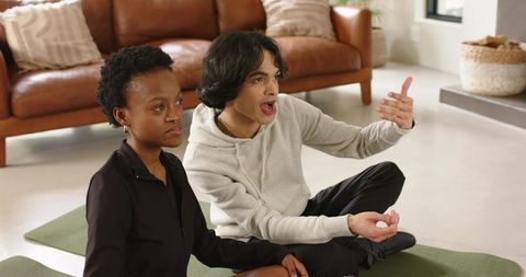 Young diverse couple practicing guided breathing on yoga mats in modern living room
