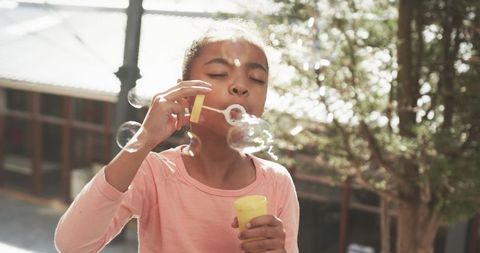 Young girl blows bubbles outdoors in sunlit yard