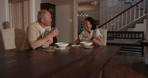 Senior Asian Couple Enjoying Drinks and Laughter at Home