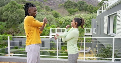 Diverse couple stretching on wooden terrace by pool for outdoor morning workout