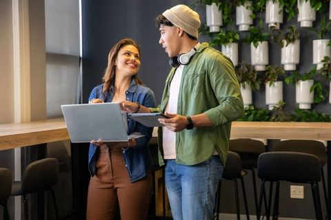 Smiling coworkers collaborating with laptop and tablet at counter in modern coworking space