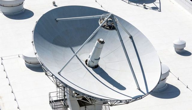 Aerial view of large white rooftop satellite dish with central feed horn and support struts