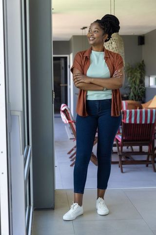 Confident young african woman standing in sunlit sunroom doorway smiling with arms crossed