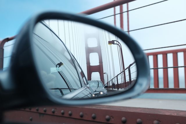 This image captures the reflection of a bridge in a car's side mirror on a foggy day, emphasizing urban travel and daily commute. Ideal for illustrating articles about transportation, urban lifestyle, or travel experiences. It can also be used in brochures promoting car safety, urban infrastructure or as part of advertisement campaigns for car insurance services and travel agencies.