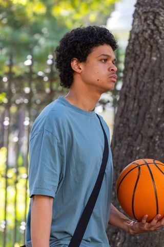 African american teen holding basketball outdoors near tree urban park lifestyle portrait
