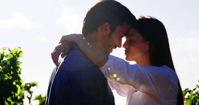 A silhouette of a young Caucasian couple sharing an intimate moment in the sunlight, with copy space. Their closeness and the warm backlighting create a romantic and serene atmosphere.