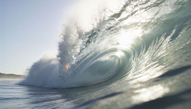 Crashing ocean barrel wave catching sunlight spray and glassy tube near shore