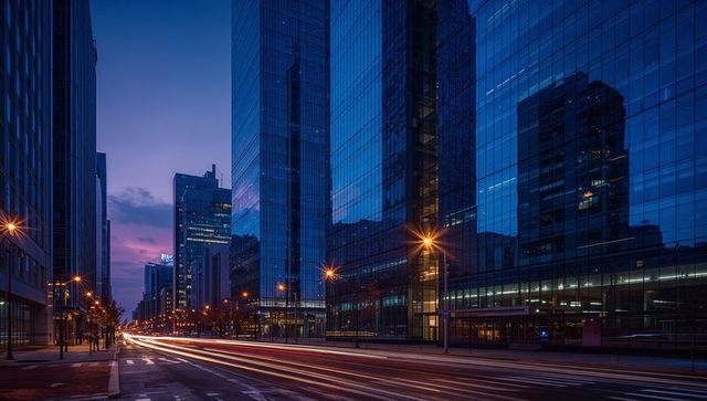 Twilight light trails along glass-fronted towers on urban avenue