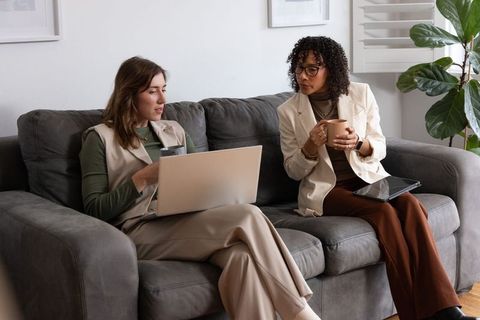 Two professional women collaborating on laptop and tablet during casual lounge meeting