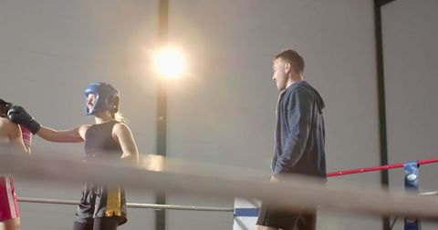 Female boxer sparring with coach in backlit boxing ring during intense training