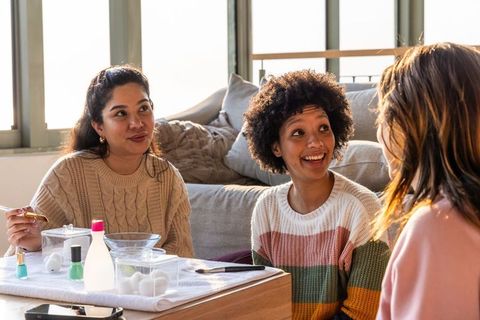 Friends sharing cozy at-home manicure session, laughing and bonding in sunlit living room