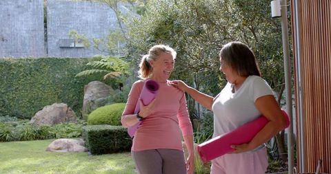 Women Greeting with Yoga Mats in Tranquil Garden Setting