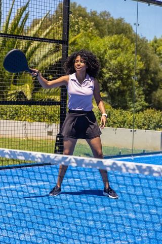 African american woman playing padel on blue court with glass enclosure and sunlit action