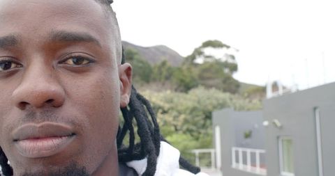 African American man wearing white hoodie gazing at camera on urban rooftop balcony