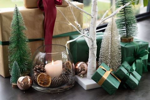 Festive christmas centerpiece with lit candle, green wrapped gifts and miniature trees