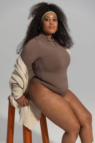Confident plus-size african american woman sitting on stool in neutral bodysuit and cardigan