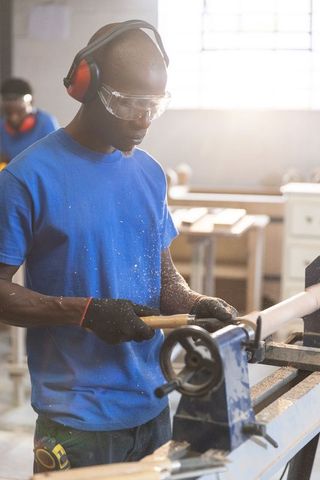 Asian man woodturning on lathe wearing goggles and earmuffs in workshop
