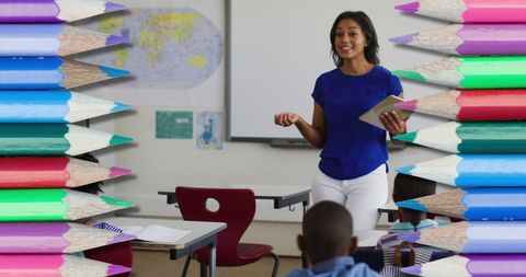 Smiling Female Teacher in Classroom Surrounded by Color Pencils