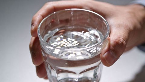 Male hands tilting glass of water creating ripples and light refraction closeup minimalist