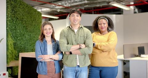 Diverse team standing confidently with arms crossed in modern office with plant wall