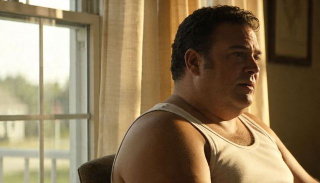 Sunlit contemplative man sitting by window wearing white tank top and thin necklace