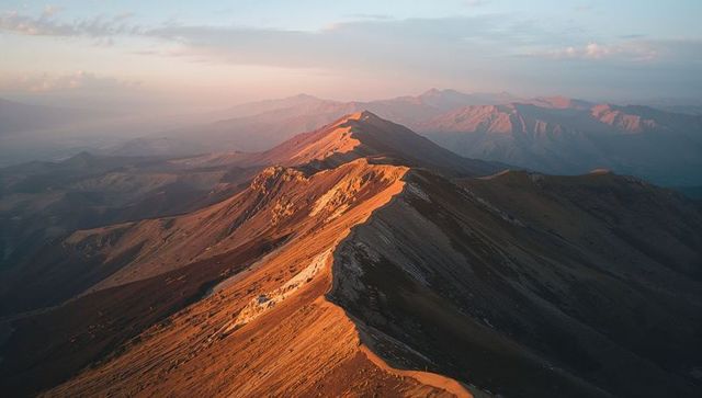 Golden hour sunlit serrated mountain ridge stretching diagonally across alpine range