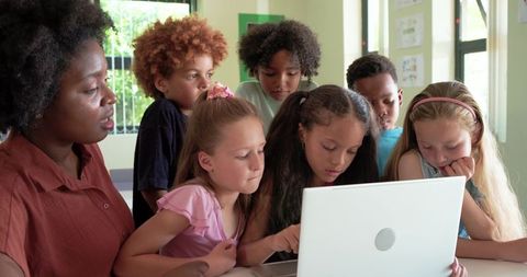African American teacher guiding diverse young students in collaborative laptop learning