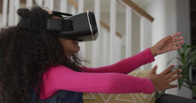 Child enjoying virtual reality experience using VR headset in living room. Ideal for illustrating the impact of technology and innovations on young generations, home entertainment, or educational tools for children.