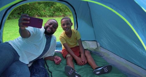 Father and son taking selfie inside tent during backyard camping and joyful bonding