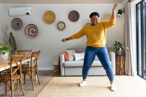 African american woman dancing with headphones in cozy boho living room with plants and rug