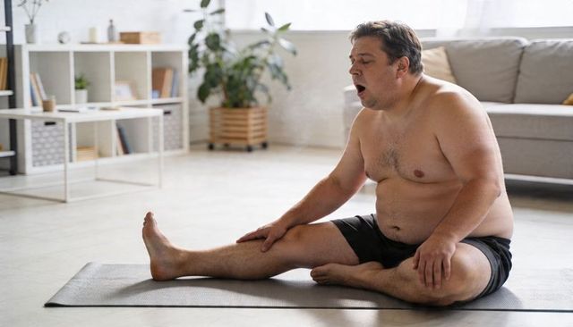 Middle-aged man stretching on yoga mat at home practicing seated hamstring and hip stretch