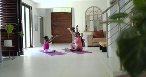 African american mother and daughter practicing yoga on purple mats in bright living room