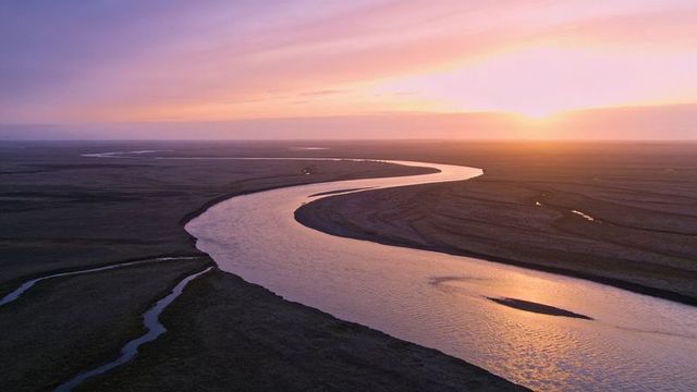 Meandering river snaking across wetland plain reflecting pastel sunset light