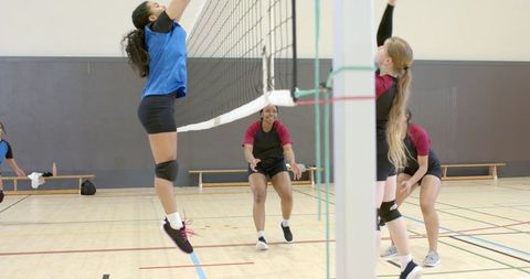 Female volleyball players jumping at net competing in indoor gymnasium teamwork and agility