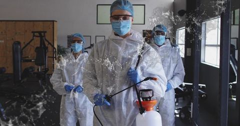 Disinfection Crew Sanitizing Gym with Pump Sprayer Wearing Full Protective Suits Masks Gloves Goggle